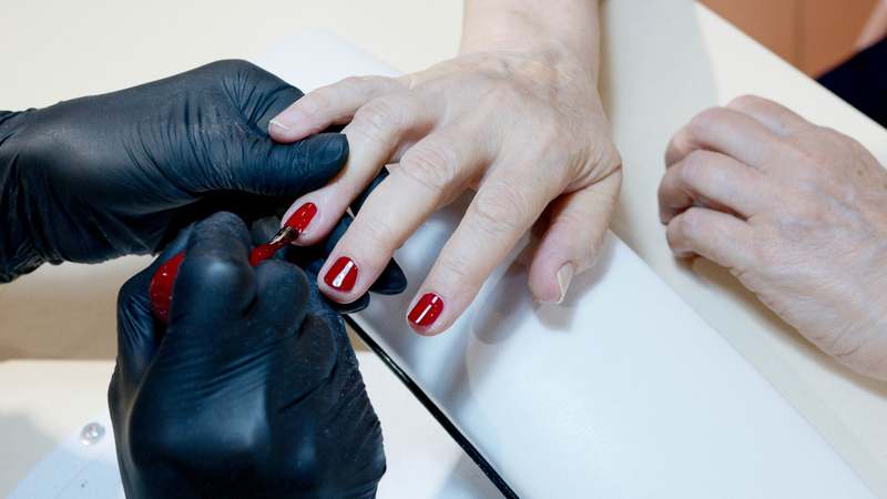 Close-up of hands applying nail polish primer to clean nails with soft-focus background of beauty tools