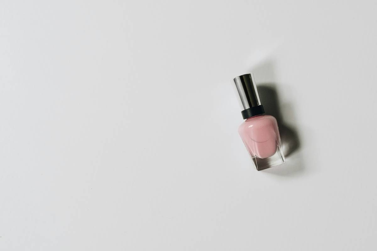 Close-up of a hand applying nail polish primer to the natural nail plate before color application – nail polish primer shown in a clear, glossy liquid form on brush