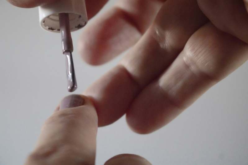 Smiling female blogger holding a curated collection of nail polish primers on a marble surface